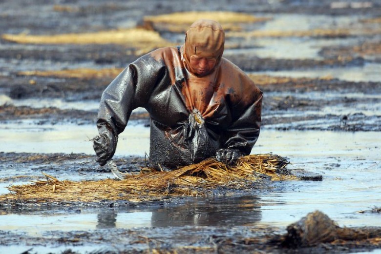 Labourer tries to clean up oil from water, Dalian, Liaoning