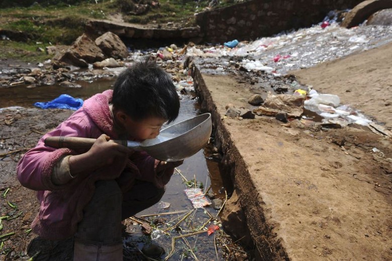 Child drinks water from stream swimming with waste in Fuyuan County, Yunnan province